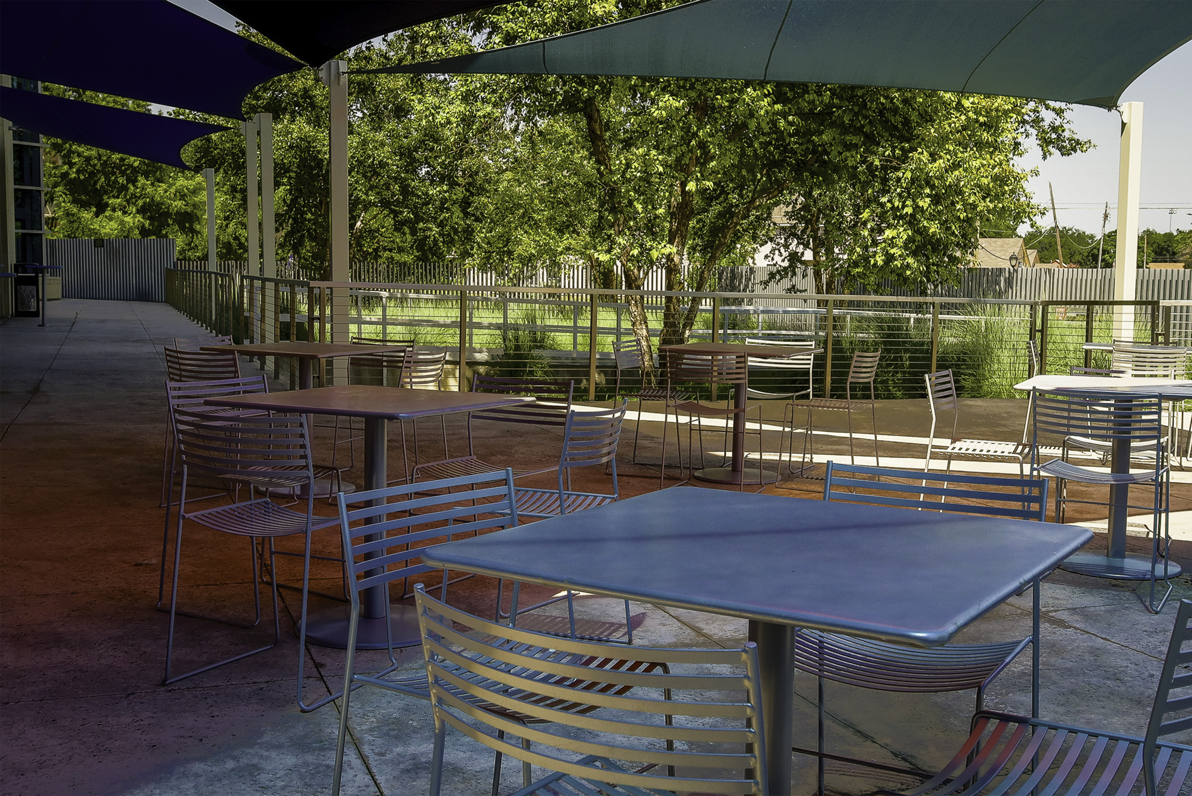 Outdoor terrace during the day. Tables and chairs set up with shade sails overhead. 